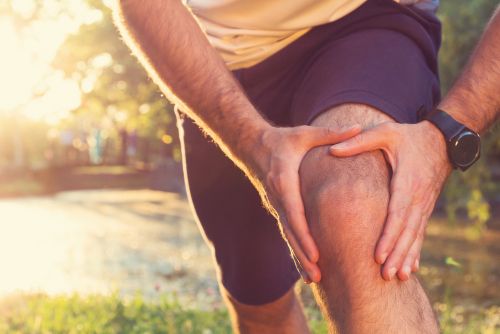 runner holding his knee from knee pain from a sports injury