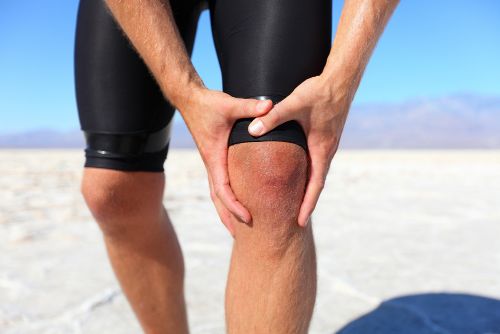 man holding his knee in pain on a beach from a running injury